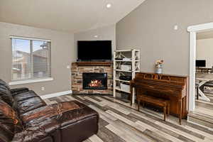 Living room with vaulted ceiling, a fireplace, and light wood-type flooring