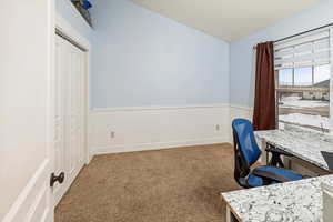 Carpeted office with lofted ceiling and a wainscoted wall