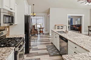Kitchen featuring appliances with stainless steel finishes, white cabinetry, light stone counters, and light wood-style flooring