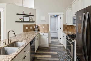 Kitchen featuring stainless steel appliances, white cabinetry, open shelves, light stone counters, and dark wood-style floors