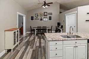 Kitchen with lofted ceiling, white cabinets, dark wood-style floors, a ceiling fan, and light stone countertops