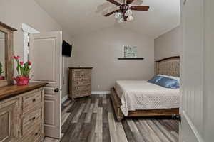 Bedroom with vaulted ceiling, dark wood finished floors, and ceiling fan