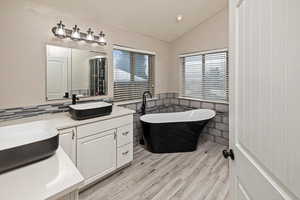 Full bathroom featuring vanity, lofted ceiling, a freestanding bath, light wood finished floors, and recessed lighting