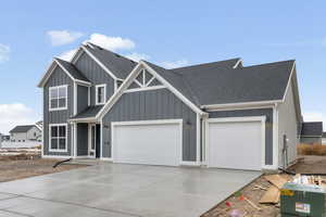 View of front of home with board and batten siding, a shingled roof, concrete driveway, and a garage