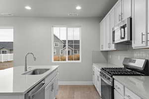 Kitchen with stainless steel appliances, light wood-type flooring, white cabinetry, light stone countertops, and recessed lighting