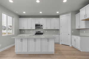 Kitchen with white cabinetry, stainless steel appliances, light stone counters, decorative backsplash, and a center island with sink