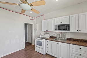 Kitchen with white electric stove, white cabinets, dark wood-style floors, black microwave, and a ceiling fan
