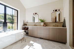 Bathroom featuring a freestanding bath, double vanity, backsplash, vaulted ceiling, and light tile patterned flooring