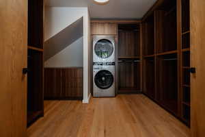 Laundry area with wooden walls, wainscoting, stacked washing machine and dryer, and light wood finished floors