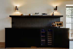 Indoor dry bar featuring dark cabinets, wine cooler, light wood-type flooring, open shelves, and glass insert cabinets