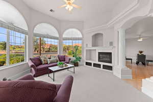 Living area featuring a ceiling fan, a glass covered fireplace, light carpet, built in shelves, and light tile patterned flooring