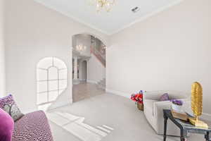 Sitting room featuring a chandelier, arched walkways, ornamental molding, carpet, and stairway