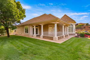 Rear view of property with stucco siding, a lawn, and covered porch