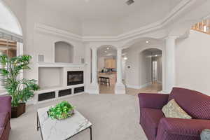 Living area with light colored carpet, arched walkways, ornate columns, and a towering ceiling