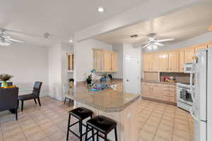 Kitchen featuring a ceiling fan, a peninsula, white appliances, light brown cabinetry, and tile countertops