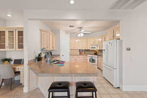 Kitchen with tile countertops, a peninsula, white appliances, light tile patterned floors, and a kitchen breakfast bar