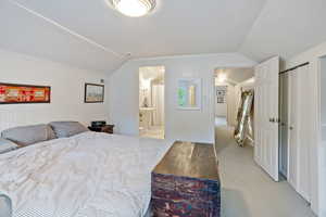 Bedroom featuring vaulted ceiling, light colored carpet, and ensuite bath