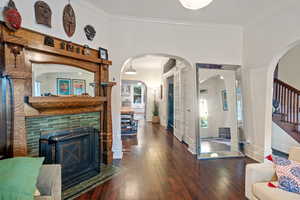 Living area featuring crown molding, dark wood-type flooring, a fireplace with flush hearth, and stairs