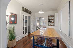 Dining room featuring arched walkways, dark wood finished floors, ornamental molding, and french doors