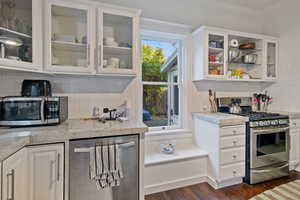 Kitchen featuring glass insert cabinets, tasteful backsplash, white cabinetry, stainless steel appliances, and light stone countertops