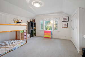 Carpeted bedroom featuring lofted ceiling and wood walls
