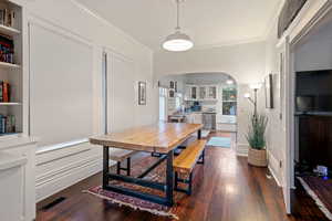 Dining space with arched walkways, dark wood finished floors, ornamental molding, and built in features
