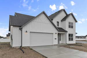 Modern inspired farmhouse with a shingled roof, board and batten siding, an attached garage, and driveway