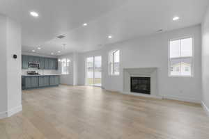 Unfurnished living room featuring recessed lighting, healthy amount of natural light, light wood-style flooring, a chandelier, and a glass covered fireplace