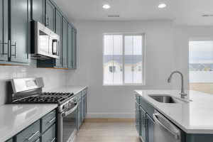 Kitchen with appliances with stainless steel finishes, recessed lighting, light wood-style floors, backsplash, and an island with sink