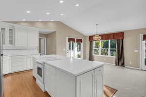 Kitchen with white range with electric cooktop, white cabinets, vaulted ceiling, glass insert cabinets.