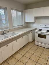 Kitchen with light countertops, electric stove, white cabinets, and light tile patterned flooring