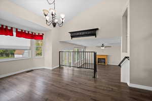 Spare room featuring a glass covered fireplace, dark wood-type flooring, high vaulted ceiling, and a chandelier