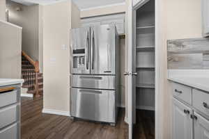 Kitchen with stainless steel refrigerator with ice dispenser, light countertops, dark wood-style floors, and ornamental molding