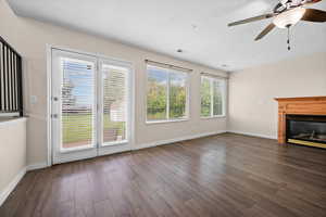 Unfurnished living room featuring plenty of natural light, ceiling fan, a glass covered fireplace, dark wood-style flooring, and a textured ceiling