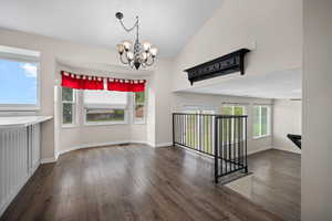 Unfurnished dining area featuring dark wood finished floors, a chandelier, and high vaulted ceiling