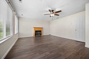 Unfurnished living room featuring a glass covered fireplace, dark wood-style flooring, and ceiling fan