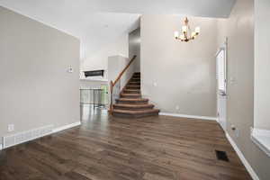 Foyer with dark wood-style flooring, healthy amount of natural light, stairs, high vaulted ceiling, and a chandelier