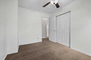 Unfurnished bedroom with dark carpet, a closet, attic access, and ceiling fan