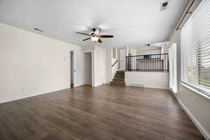 Unfurnished living room featuring stairway, dark wood-style floors, ceiling fan, and a textured ceiling
