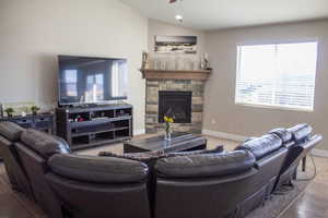 Living room featuring vaulted ceiling, a stone fireplace, wood finished floors, and a ceiling fan
