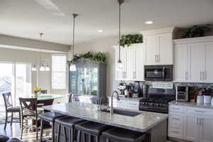 Kitchen with stainless steel appliances, white cabinets, light stone countertops, a kitchen breakfast bar, and recessed lighting