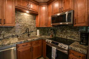 Kitchen with stainless steel appliances, decorative backsplash, brown cabinets, and dark stone counters