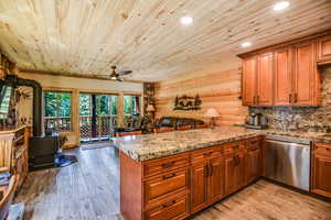 Kitchen featuring a wood stove, brown cabinets, open floor plan, dishwasher, and wooden ceiling