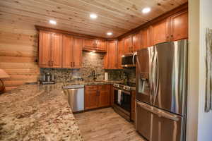 Kitchen with appliances with stainless steel finishes, brown cabinetry, light stone countertops, light wood-style flooring, and decorative backsplash
