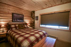 Carpeted bedroom with a baseboard radiator, log walls, and wood ceiling