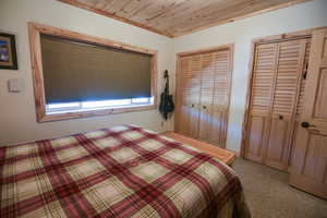 Bedroom with multiple closets, wooden ceiling, light carpet, and ornamental molding