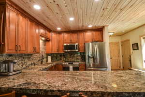 Kitchen with stainless steel appliances, brown cabinets, dark stone counters, recessed lighting, and tasteful backsplash