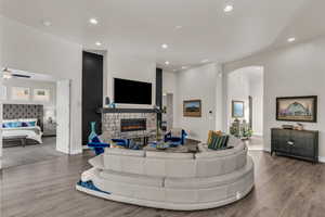 Living room with recessed lighting, wood finished floors, arched walkways, and a stone fireplace