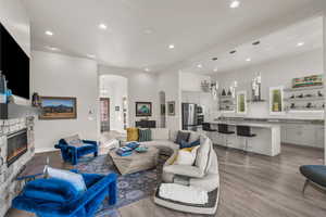 Living area featuring arched walkways, a stone fireplace, light wood finished floors, recessed lighting, and a towering ceiling