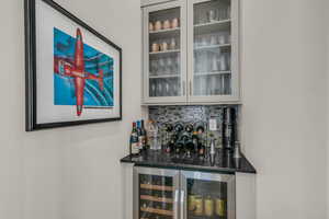 Indoor dry bar featuring glass insert cabinets, wine cooler, and dark stone counters